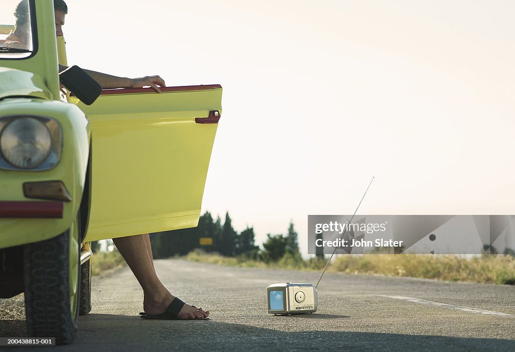 Man in car watching portable television through open door, side view