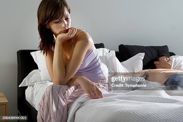 young woman sitting on bed, man sleeping in background - couple in bed fotografías e imágenes de stock