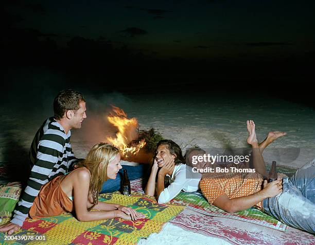 two couples relaxing on beach beside camp fire, dusk - allongé sur le devant photos et images de collection
