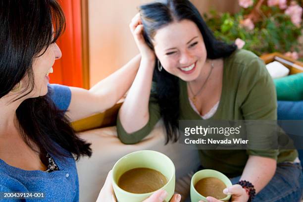 mother and daughter having coffee on sofa, daughter laughing - family on couch with mugs stock pictures, royalty-free photos & images