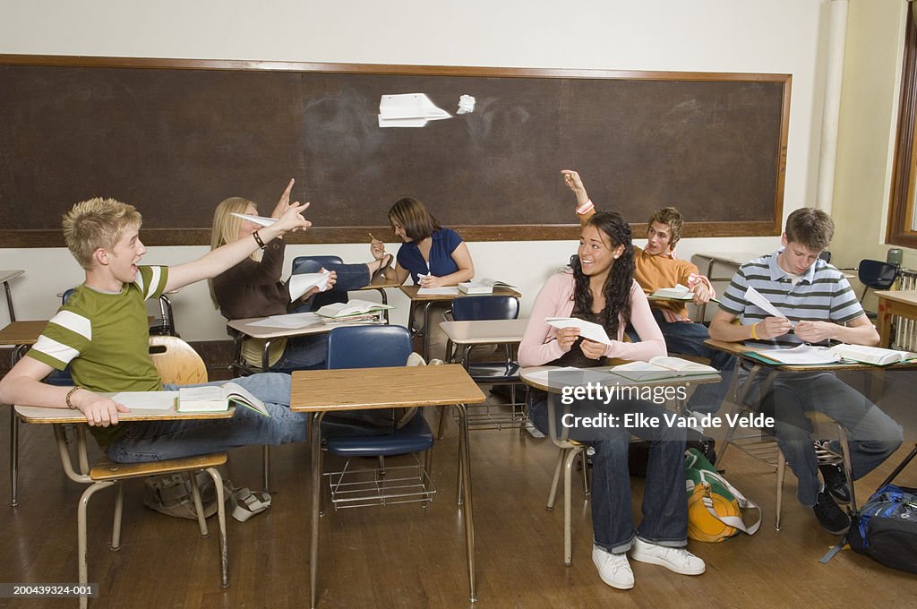 Six teenagers (16-18) throwing paper airplanes in classroom