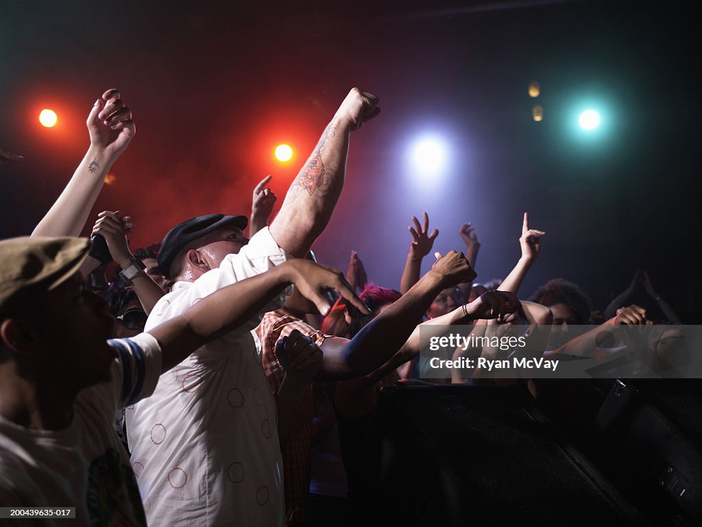 Crowd cheering in front of stage in nightclub, arms raised, side view