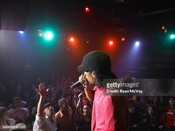 man singing on stage in nightclub, crowd raising arms in background - rockstar stock-fotos und bilder