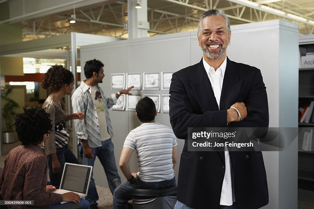 Mature businessman, portrait, others looking at designs in background