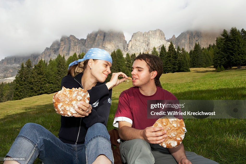 Italy, Alto Adige, young couple sitting in valley eating bread