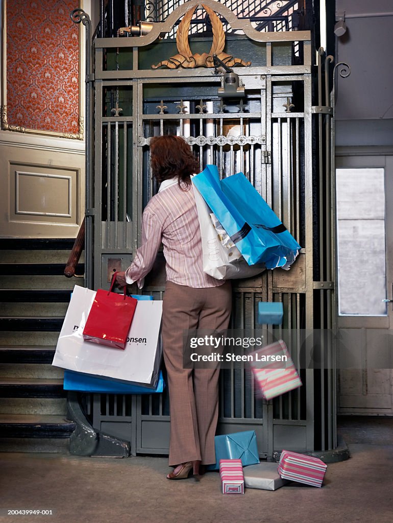 Woman pressing lift button, holding shopping bags, rear view