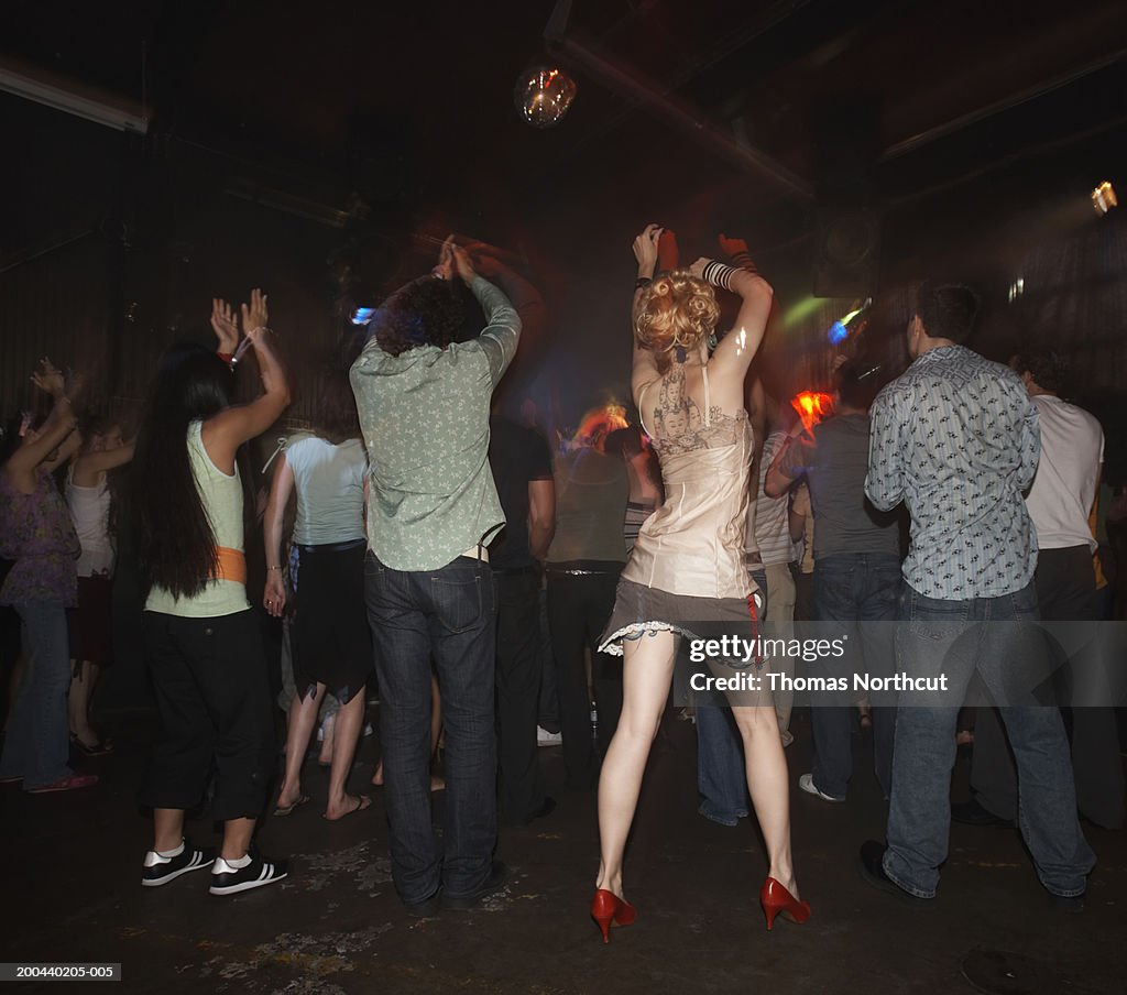 Group of adults dancing in nightclub, arms raised, rear view