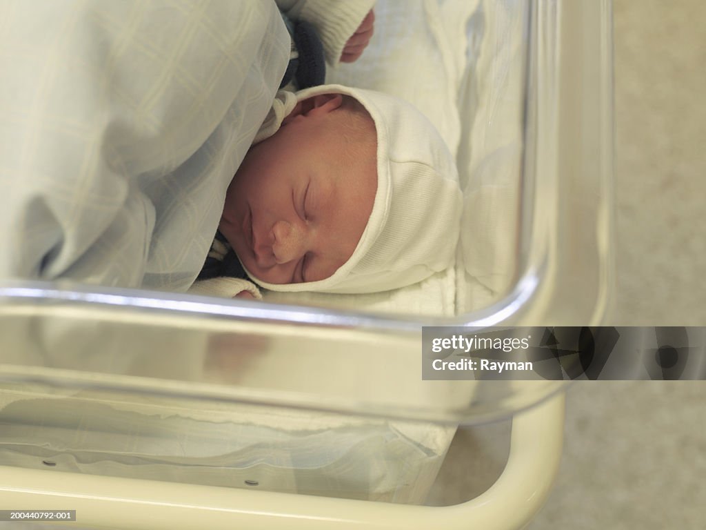 Newborn baby boy sleeping in hospital cot, overhead view