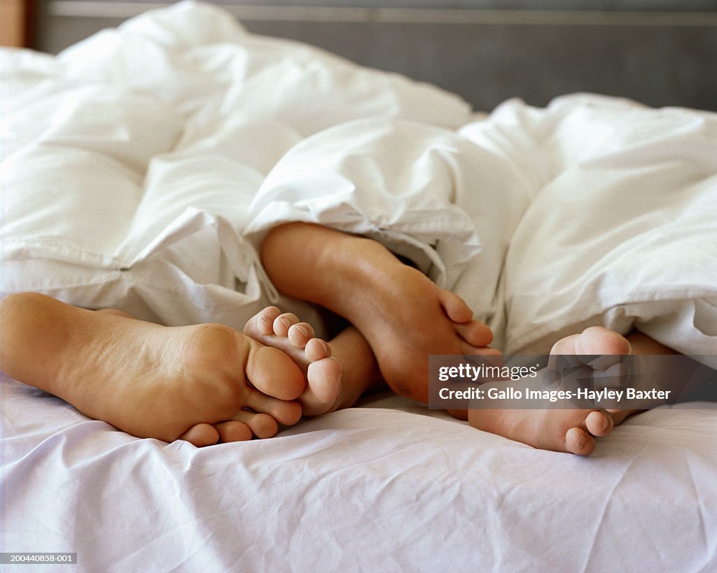 Feet of couple sticking out from under duvet, close up