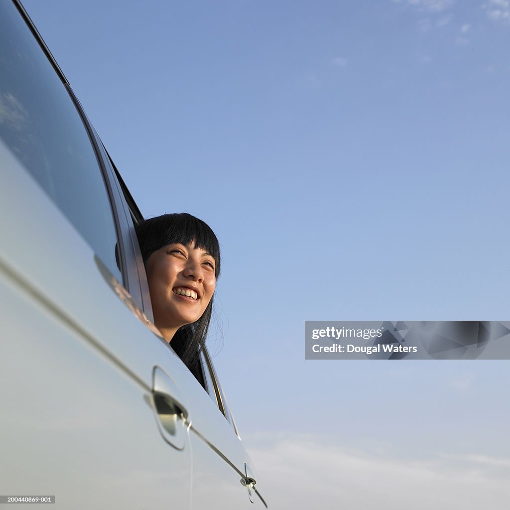 Young woman looking out of car window, smiling, low angle view