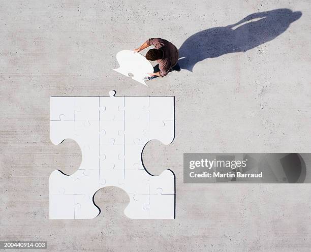 man placing jigsaw piece into jigsaw, overhead view - big puzzle photos et images de collection