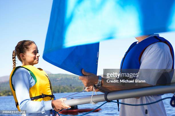 girl (13-15) holding boom while father adjusts sail on boat by lake - sail boom stock-fotos und bilder