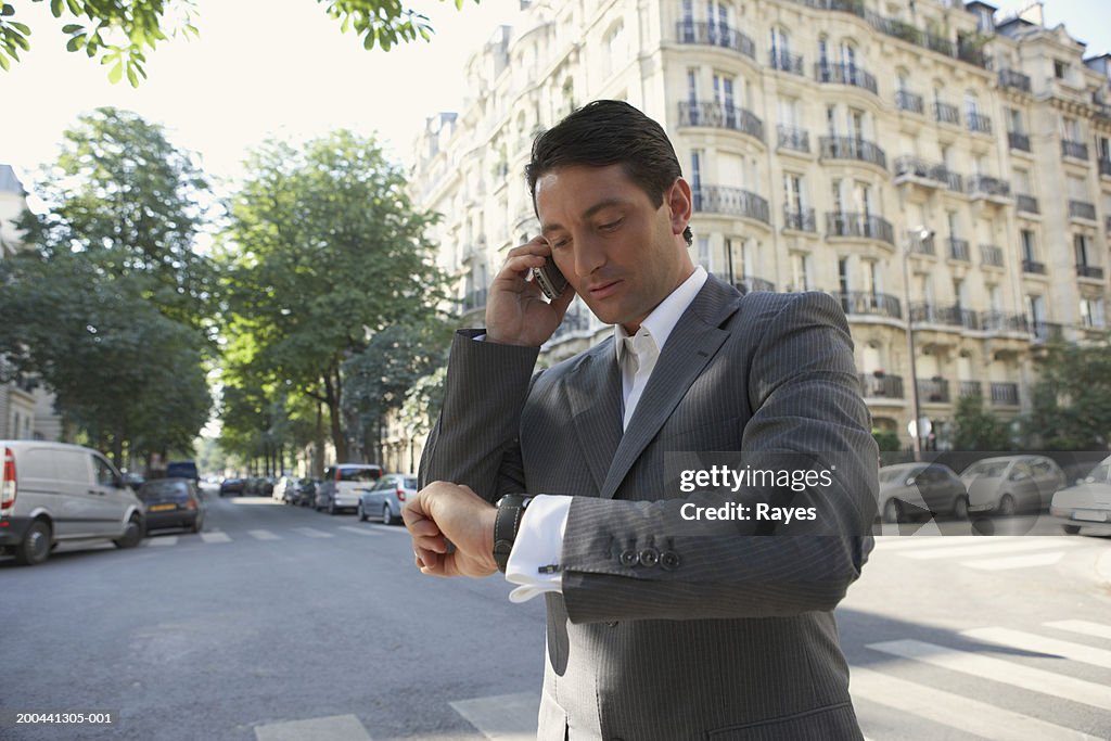 France, Paris, man using mobile phone in street, checking watch