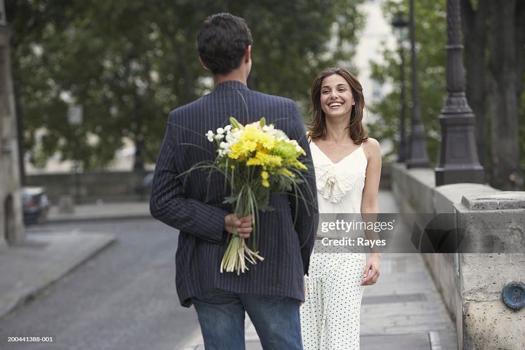 France, Paris, young couple outdoors, man holding flowers behind back