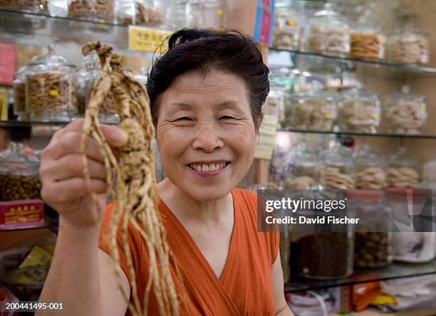 senior woman holding ginseng root in herbal medicine store, portrait - ginseng stock-fotos und bilder