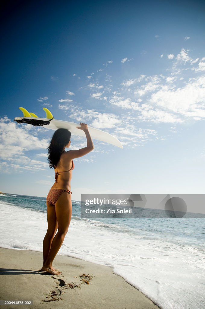 Young woman balancing surboard on head at beach, side view