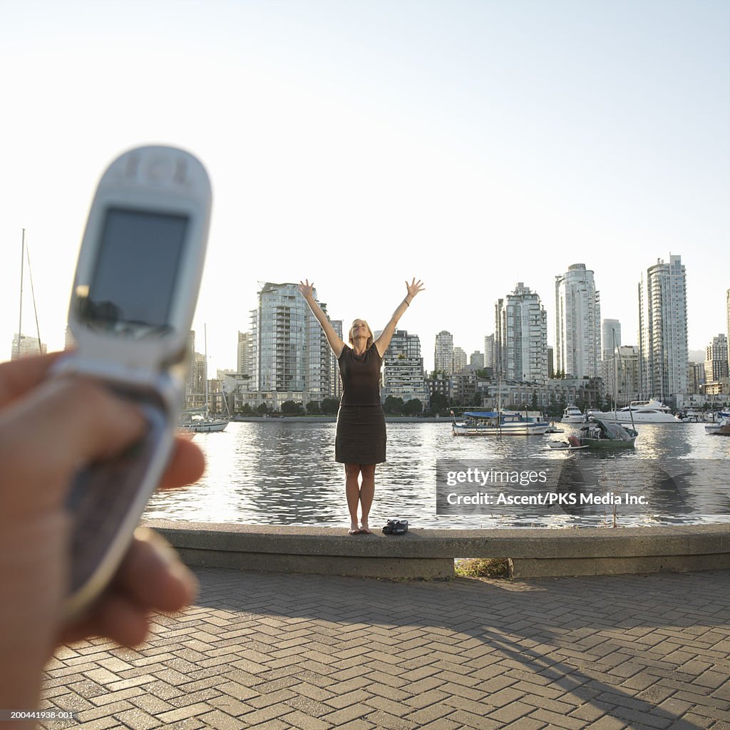 Couple on waterfront, man photographing woman with camera phone