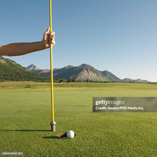 man holding flag pole by golf ball rolling into hole, close-up - holding flag stock pictures, royalty-free photos & images