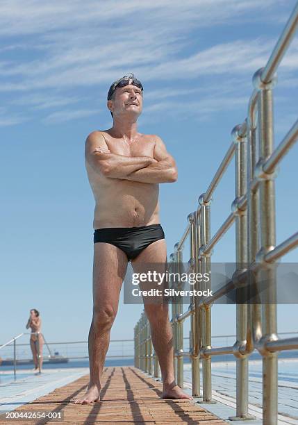 senior man standing by outdoor swimming pool, arms crossed - calções de corrida imagens e fotografias de stock