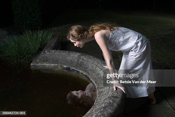 teenage girl (16-18) leaning over reflection in garden pond, night - presumir fotografías e imágenes de stock