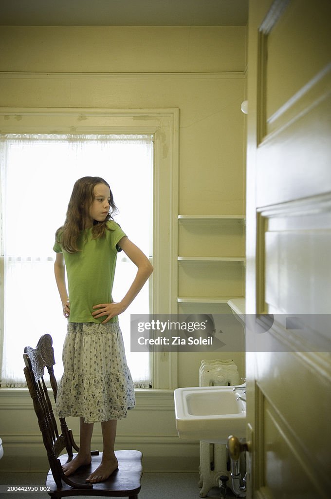 Girl (7-9) standing on chair, looking over shoulder in mirror