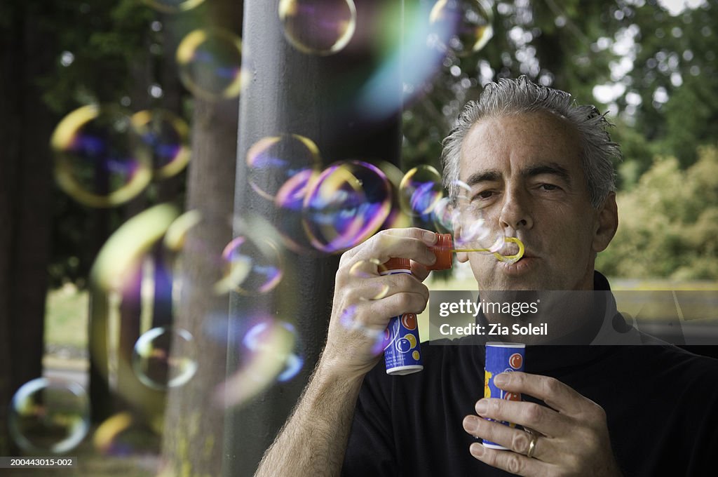Mature man blowing soap bubbles on porch