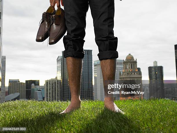 businessman carrying shoes in grass field (low section) - barefoot men stock-fotos und bilder