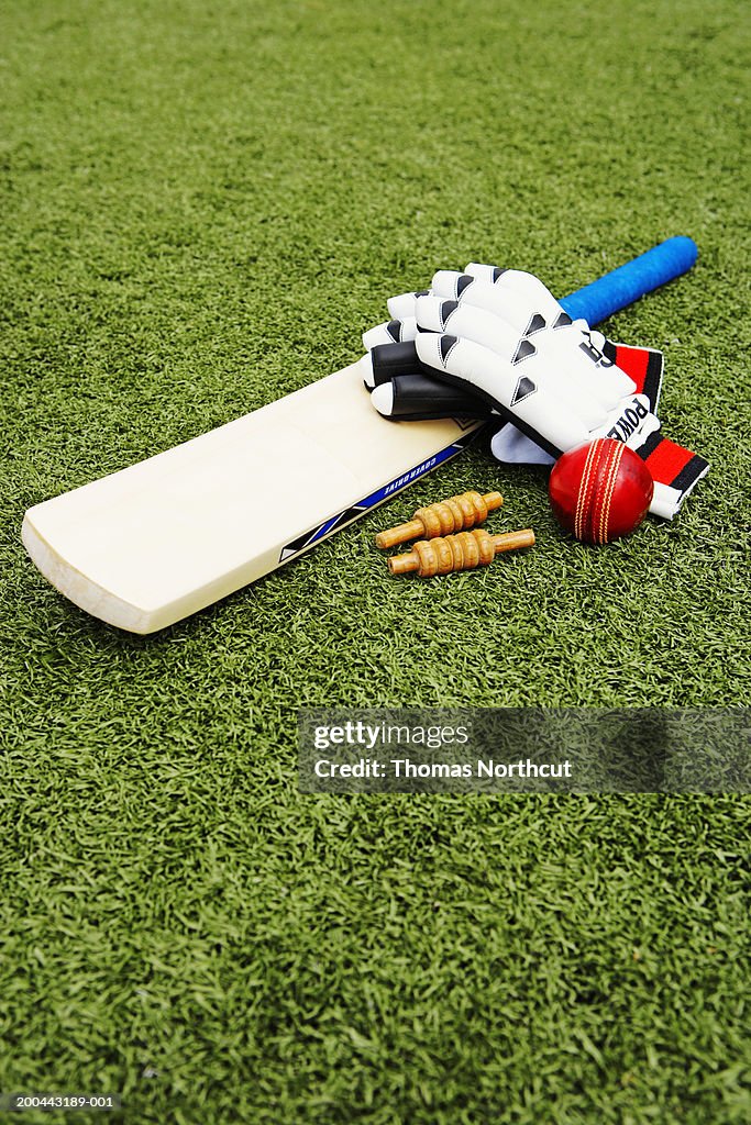 Cricket bails, bat, ball and gloves on artificial turf, elevated view