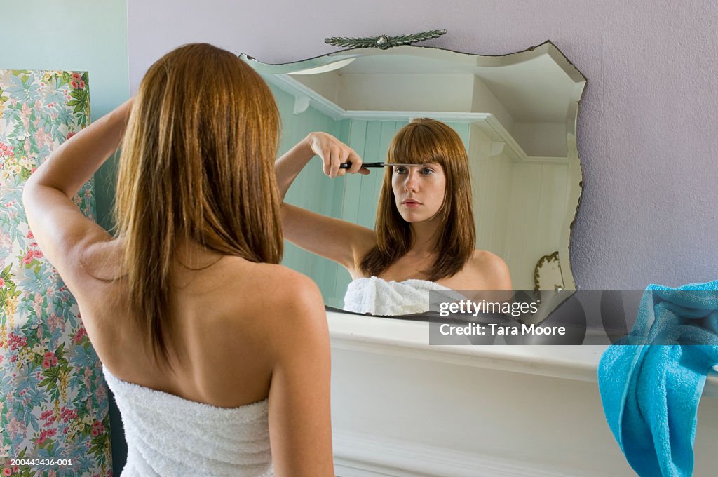Young woman wearing towel cutting fringe in mirror, rear view