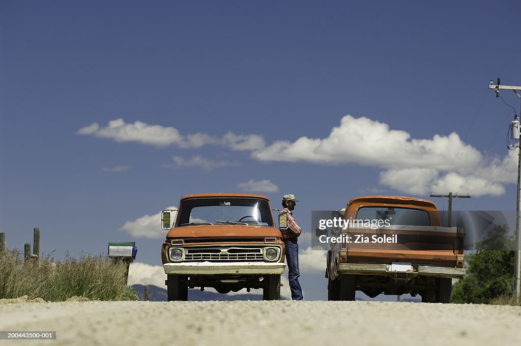 Two pick-up trucks stopping on dirt road, people talking