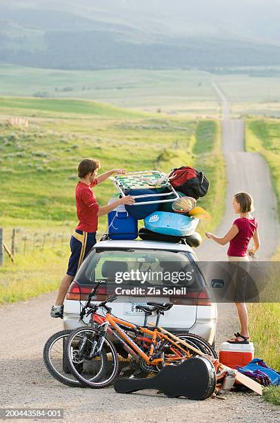 young couple packing car with vacation gear on empty road - over burdened stock pictures, royalty-free photos & images