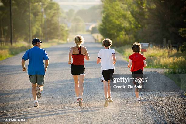 parents and sons (11-14) running on gravel road, rear view, summer - run shirt stock-fotos und bilder