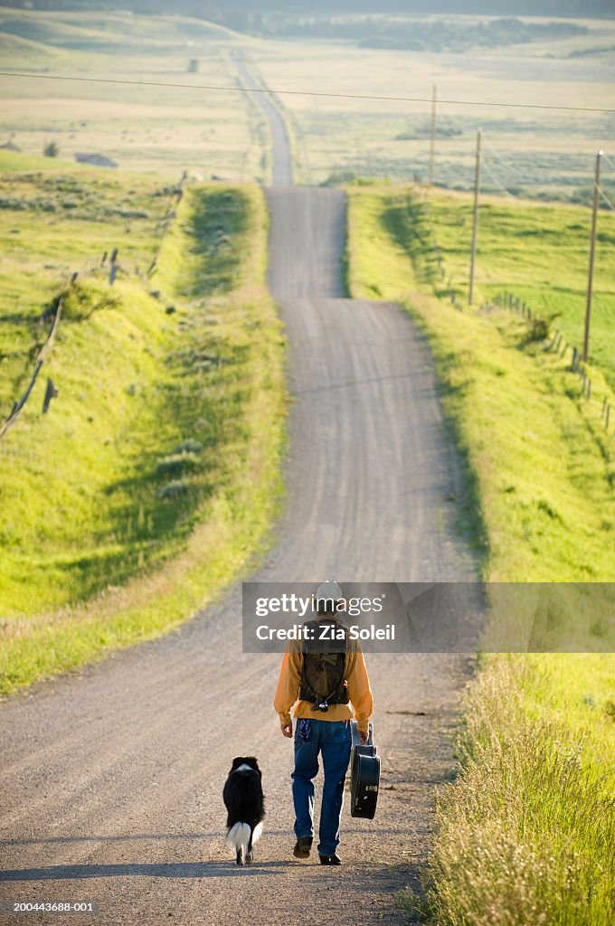 Young man walking with dog down rural road, rear view