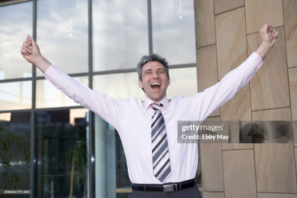 Mature businessman cheering, arms raised, close-up