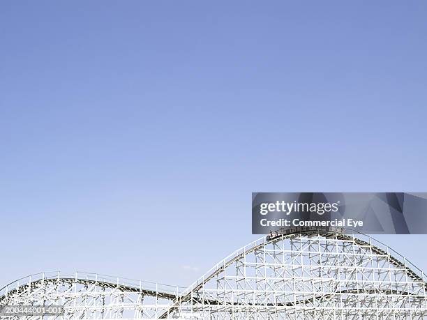 rollercoaster with people raising arms in air in cars on top - parque de diversiones fotografías e imágenes de stock