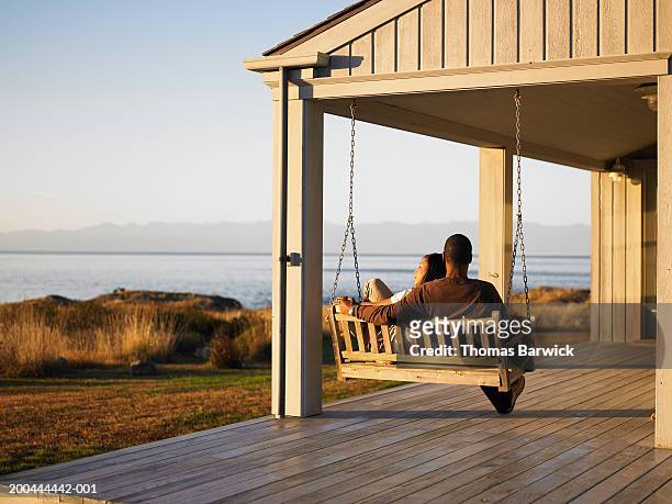 couple sitting on porch swing overlooking water, dusk, rear view - back porch stockfoto's en -beelden