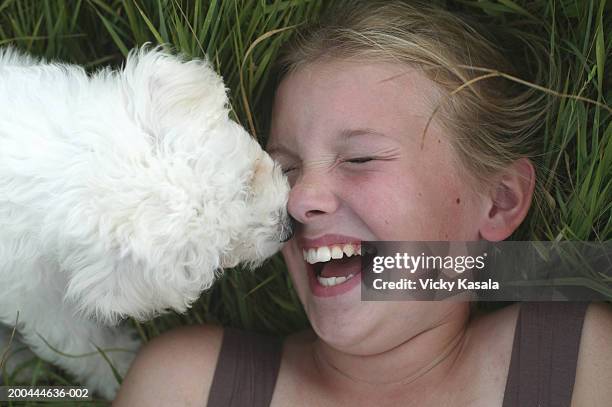 Girl (10-12) lying in grass, puppy licking face, laughing