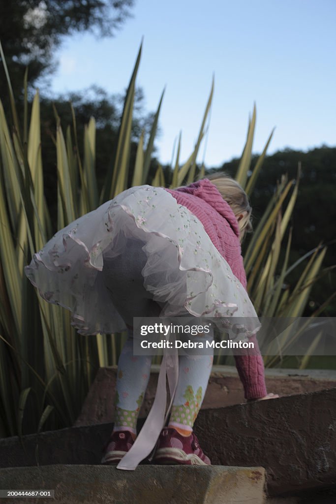 Girl (4-6) wearing frilly skirt and pink sweater climbing up steps