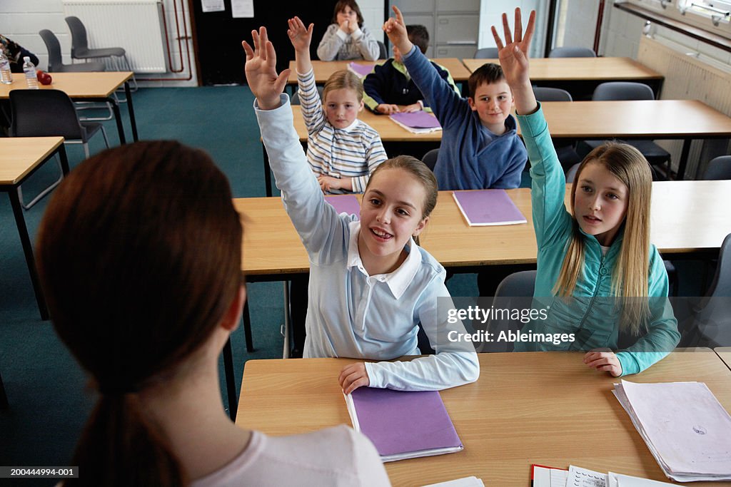Schoolchildren (7-11) in classroom, four with raised hands