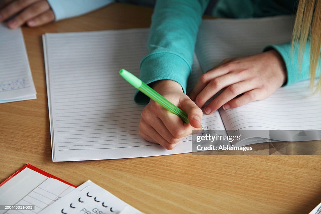 Two schoolgirls (10-12) writing in exercise books, close-up