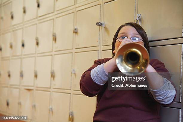 schoolboy (8-10) playing trumpet, leaning against lockers, portrait - wind instrument stock pictures, royalty-free photos & images