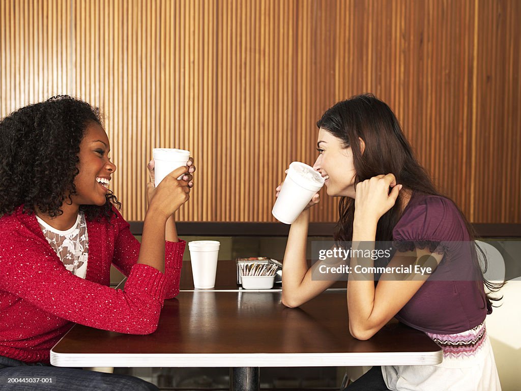 Two young women at restaurant table smiling, side view