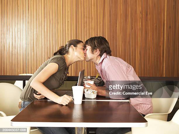 young couple kissing across restaurant table, side view - young couple kiss ストックフォトと画像