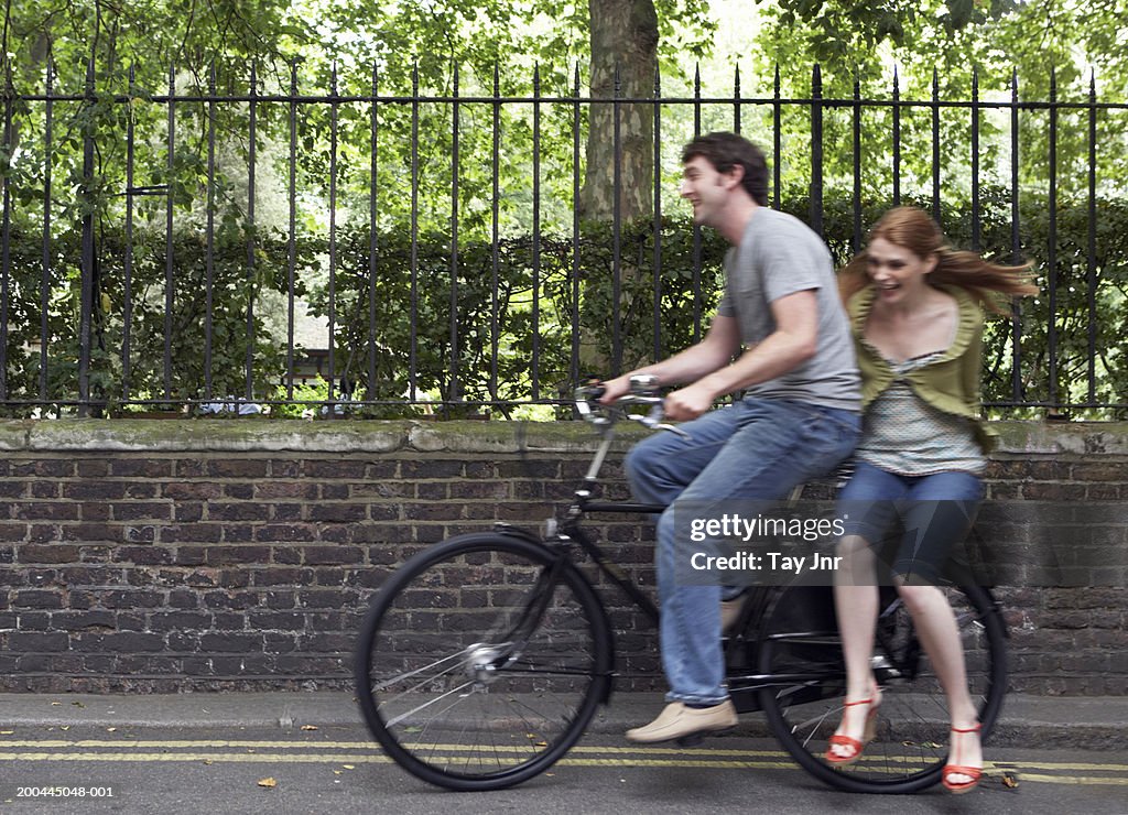 Young woman taking ride on back of man's bike (blurred motion)