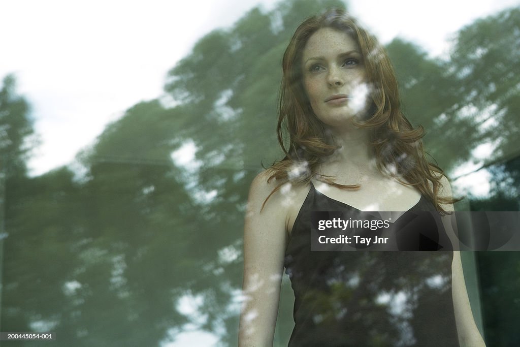 Young woman looking out of window, trees reflected in glass