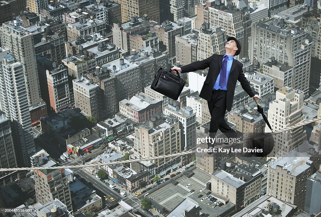 Businessman with umbrella and briefcase on tightrope over cityscape