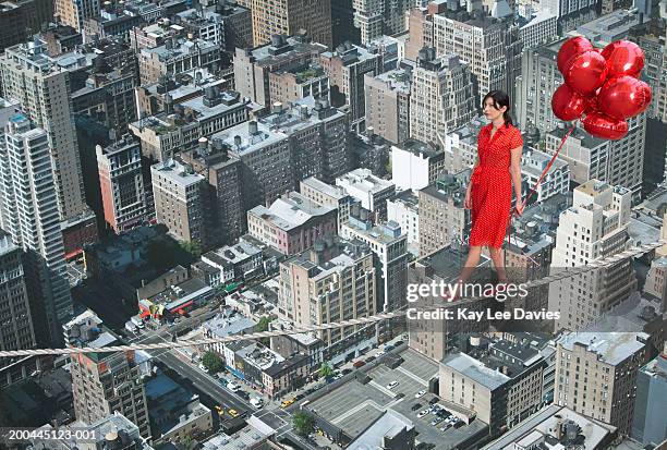 young woman holding bunch of balloons, on tightrope over cityscape - woman tightrope stock pictures, royalty-free photos & images