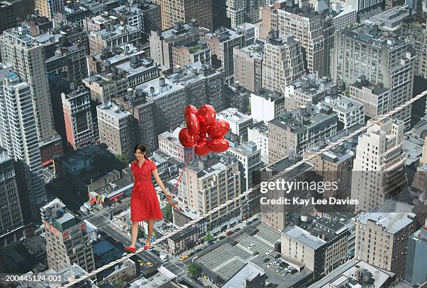 young woman holding bunch of balloons, on tightrope over cityscape - woman tightrope stock pictures, royalty-free photos & images