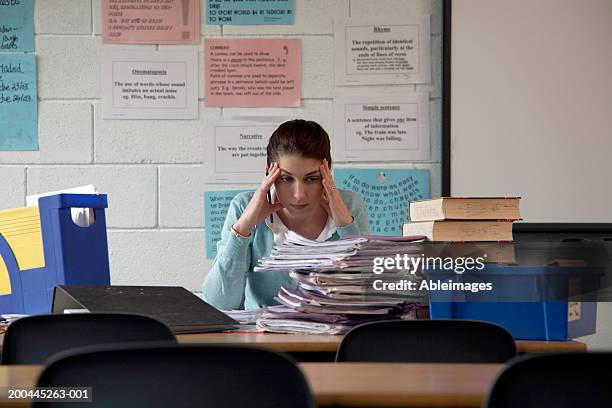 schoolteacher at desk staring at piled exercise books, hands to head - colorgrading stock-fotos und bilder