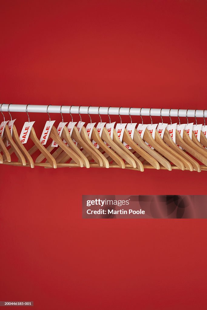 Rail of clothes hangers with sale tags attached,against red background